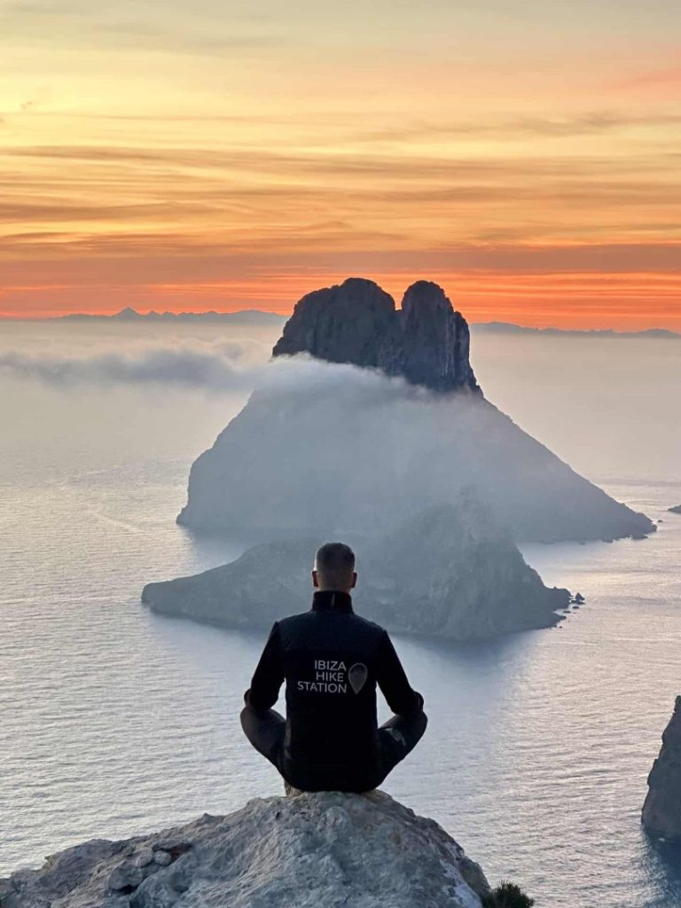 Hiker meditating at sunrise overlooking mystical Es Vedrà island on Ibiza’s Mystical Hike Station coastal trail