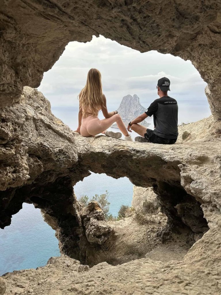 Hikers resting in a natural rock cave overlooking mystical Es Vedrà island on Ibiza’s Mystical Hike Station coastal trail