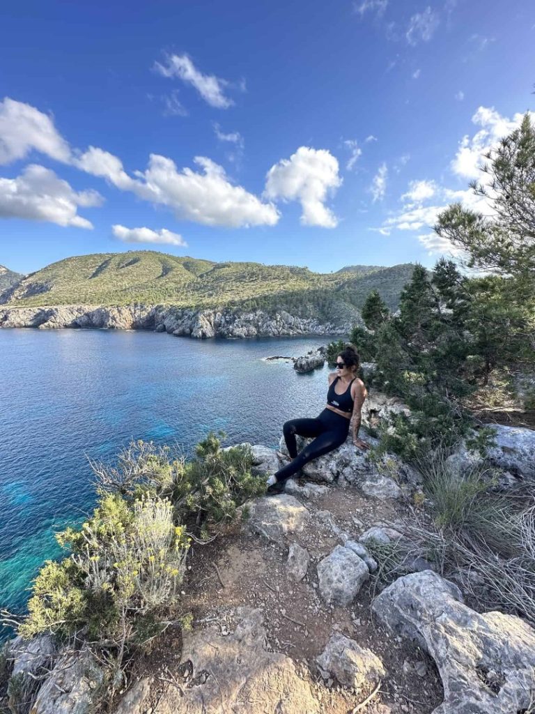 Hiker relaxing on cliff with turquoise Mediterranean view during Azure Hike Station coastal hike in Ibiza