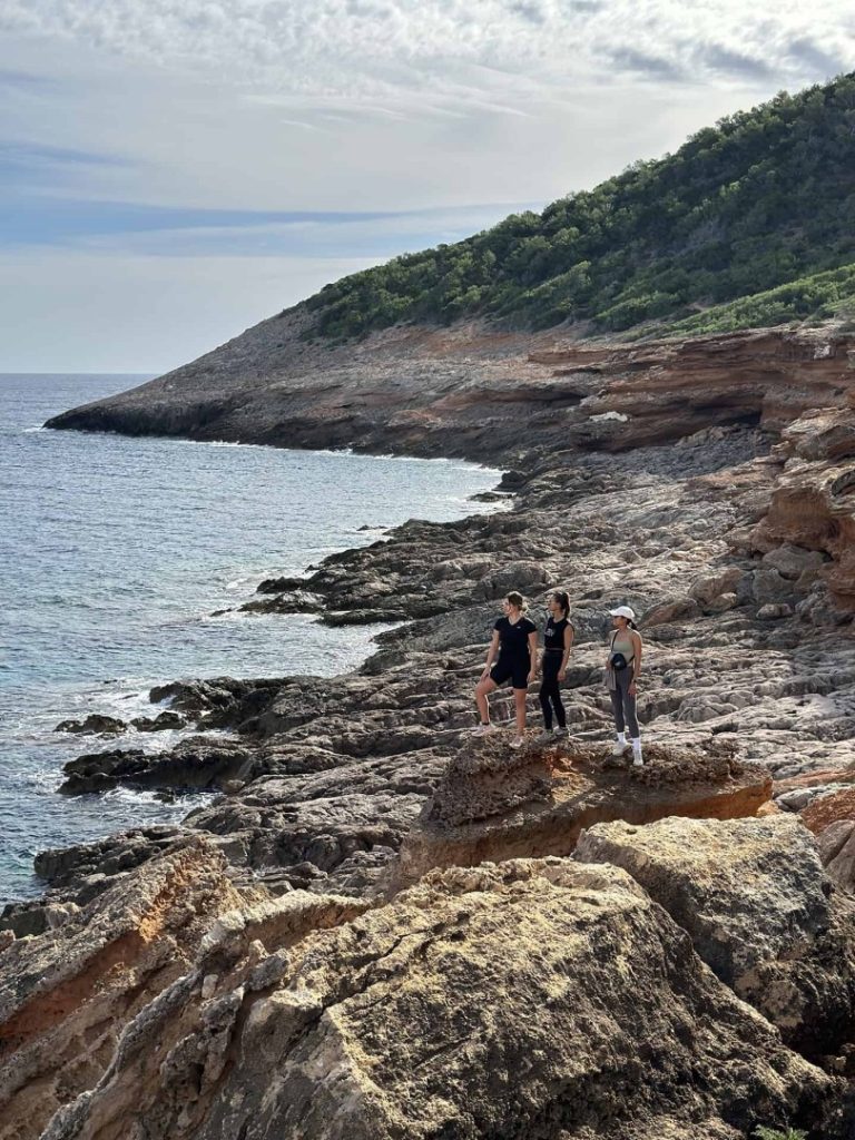 Hikers exploring rugged coastline on Ibiza’s Deus Hike Station trail with rocky cliffs and Mediterranean sea views