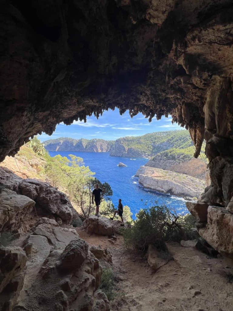 Hikers standing in sea cave overlooking Ibiza coastline during Evergreen Hike Station coastal hiking adventure