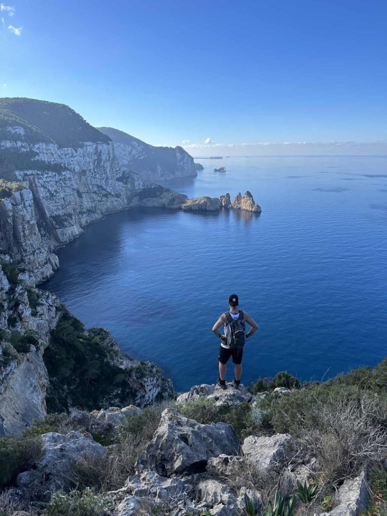 Hiker overlooking dramatic cliffs and deep blue Mediterranean fjord coastline on Ibiza’s Fjord Hike Station advanced trail