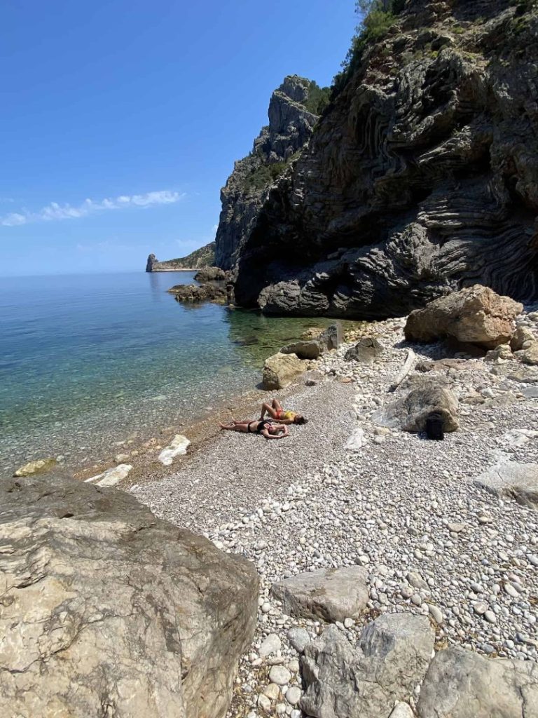 Hikers sunbathing on a hidden beach with turquoise waters along the Sardine Hike Station coastal hiking route in Ibiza