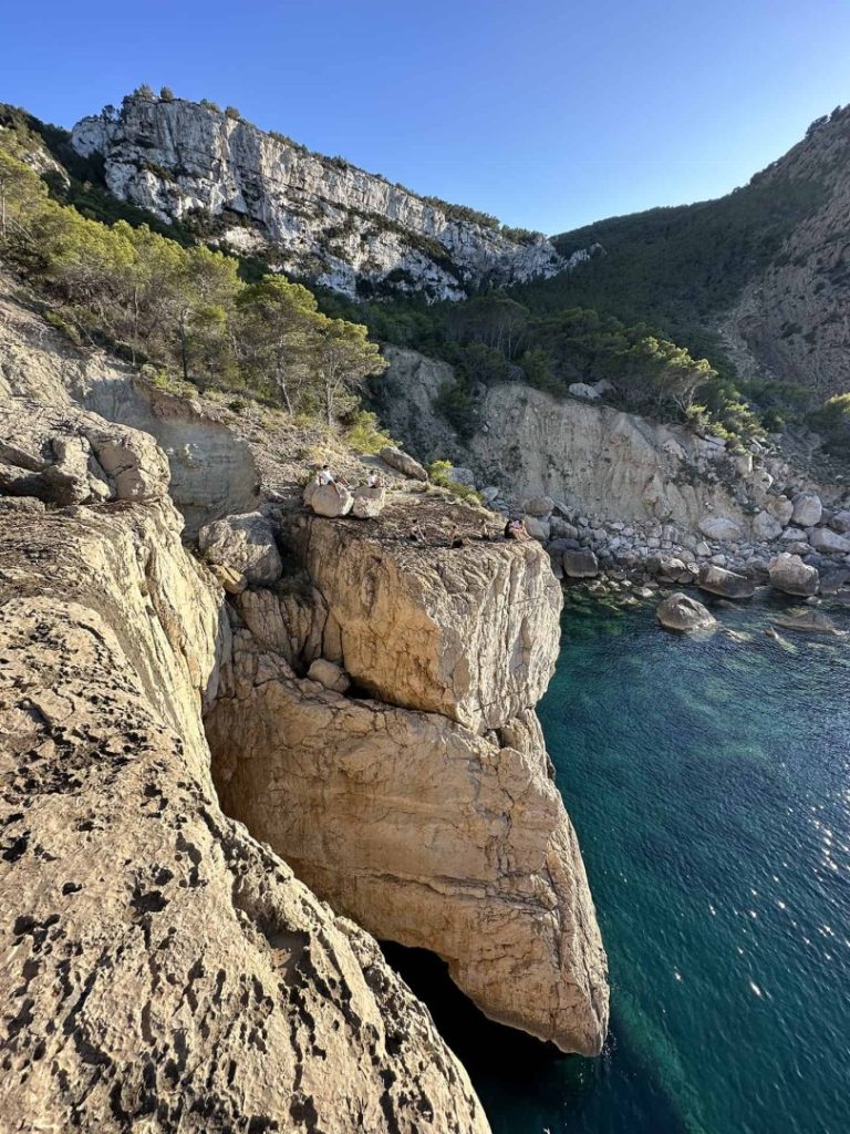 Hikers enjoying the view on limestone cliffs above turquoise sea on Ibiza coastal hike.
