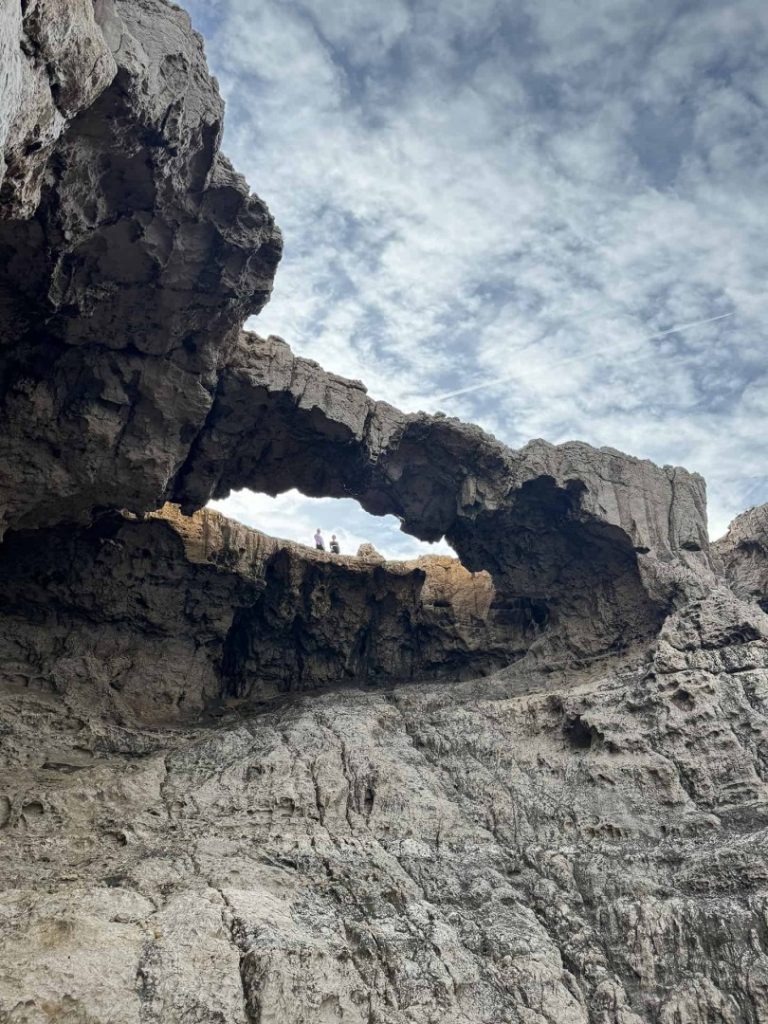 Hikers standing on natural rock arch above rugged cliffs on Ibiza Arch Hike trail with dramatic coastal limestone formations