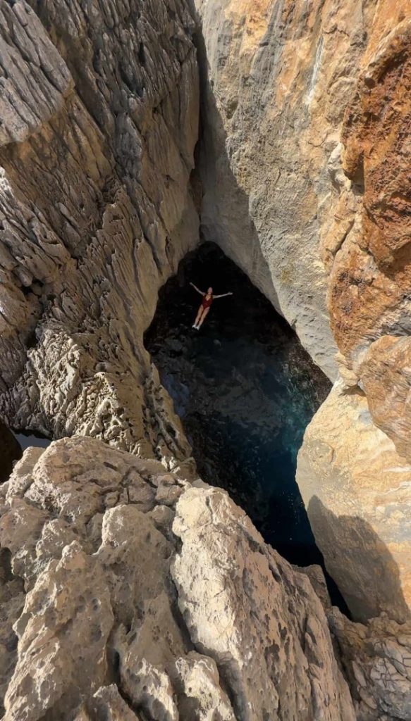 Hiker swimming in hidden rock pool inside coastal cave on Ibiza Hike trail with dramatic cliffs and turquoise water