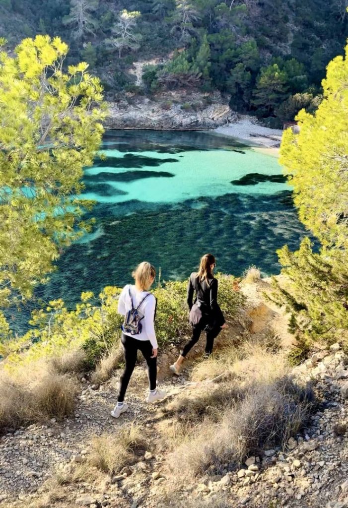 Hikers descending coastal trail to turquoise beach during Beach Hike Station scenic coastal hike in Ibiza