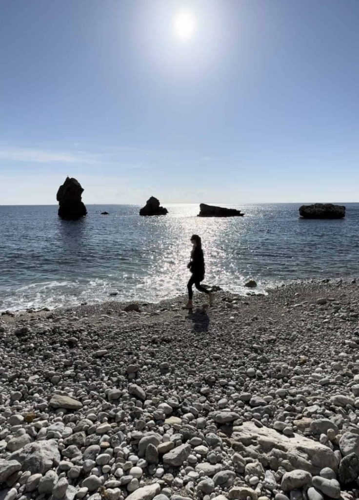 Hiker walking along rocky beach with sea stacks during Beach Hike Station coastal hiking adventure in Ibiza