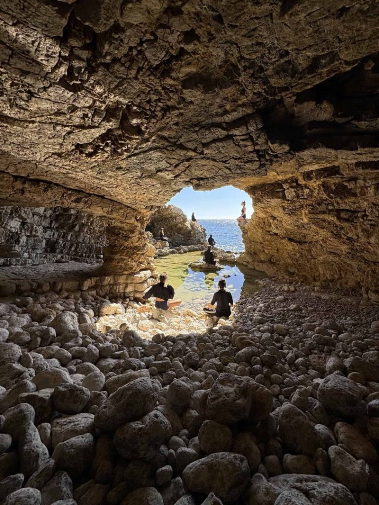 Hikers meditating inside sea cave with a view of Ibiza coast during Nobu Hike Station scenic coastal hike