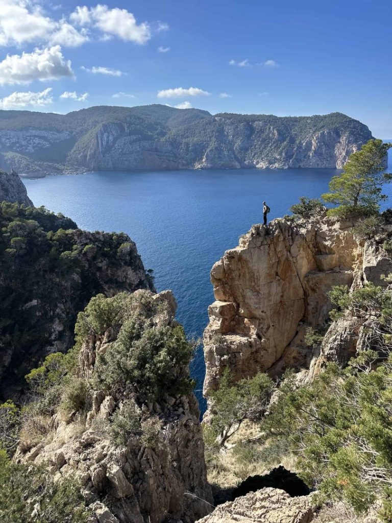 Hiker standing on dramatic cliff viewpoint overlooking Mediterranean sea during Quelona Hike Station coastal hike in Ibiza