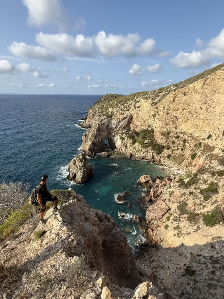 Amante Hike: Scenic coastal hike in Ibiza showing a hiker looking over a stunning bay with clear blue water and rugged cliffs.