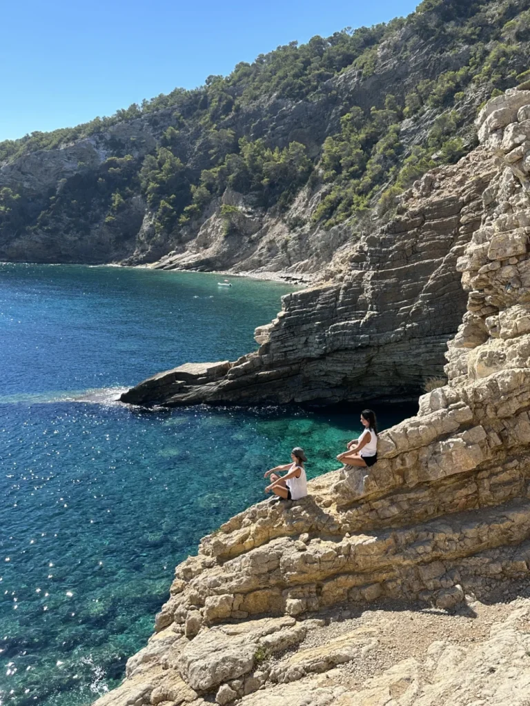 Hikers resting on limestone cliffs above turquoise waters on Ibiza’s scenic and unique Marko Hike Station coastal trail