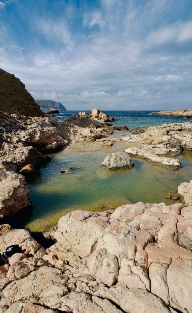 A hiker resting and swimming in a cove along the easy coastal walking trail of Moon Hike