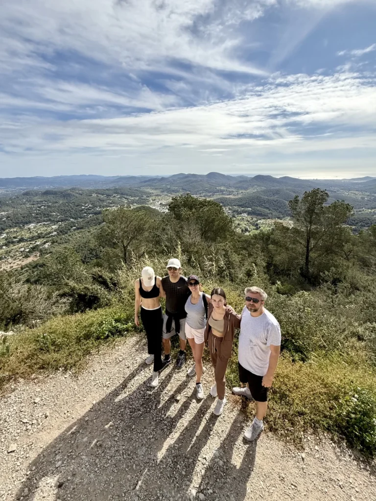 Group of hikers posing together on a sunny mountain trail at the summit hike station, overlooking beautiful green valleys.